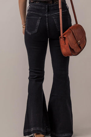 Rear view of woman wearing Bella Road Button-Fly Flare Jeans with Pockets in black, paired with a brown leather crossbody bag