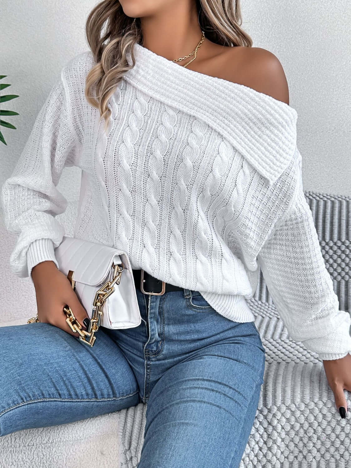 Woman wearing Bella Road Cable-Knit One Shoulder Long Sleeve Sweater in white paired with blue jeans.