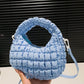 Blue quilted puffy crossbody bag with removable strap held in hand against a dark background.