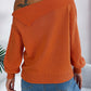 Woman wearing Bella Road orange cable-knit one-shoulder long sleeve sweater with blue jeans.