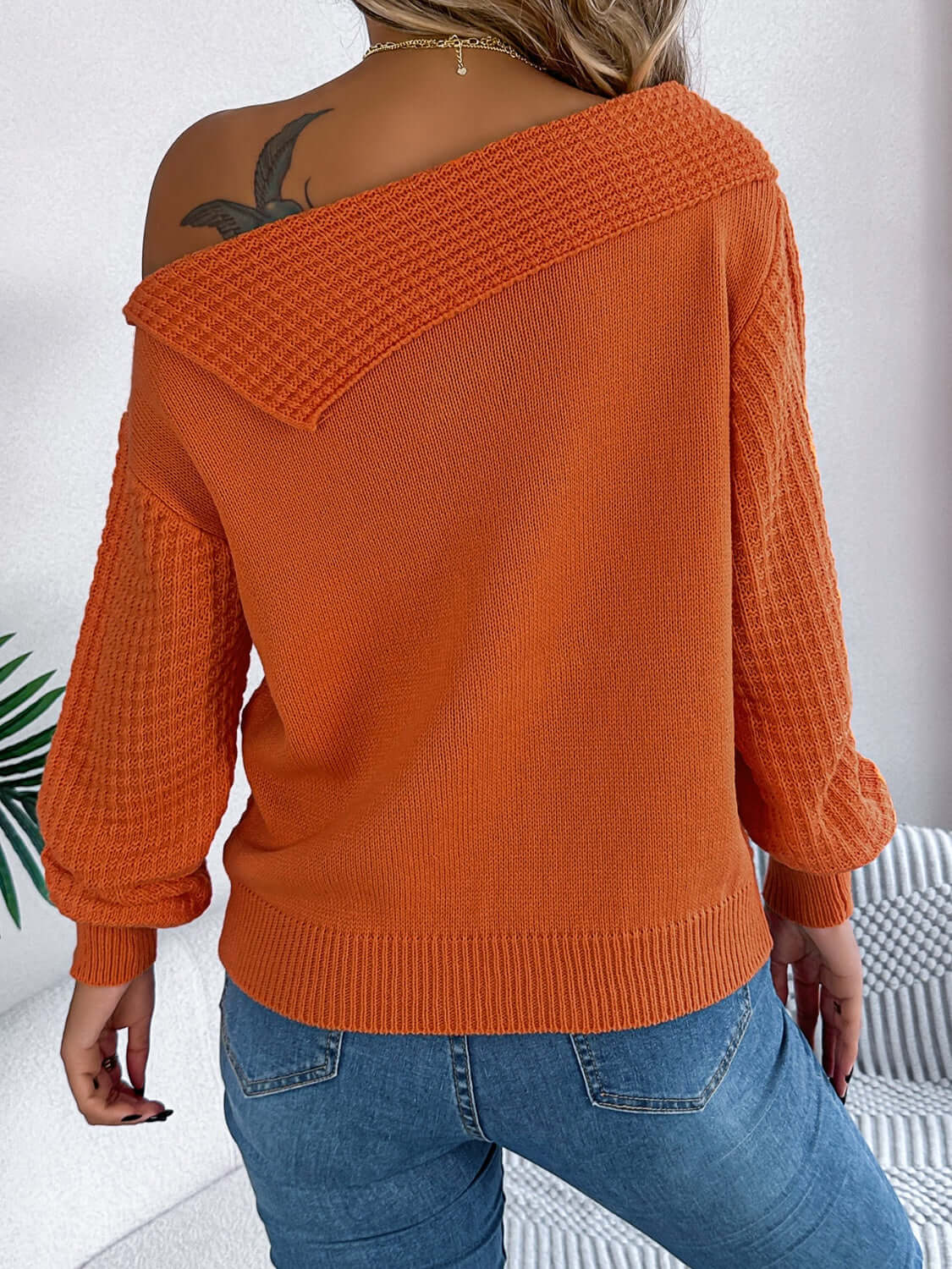 Woman wearing Bella Road orange cable-knit one-shoulder long sleeve sweater with blue jeans.