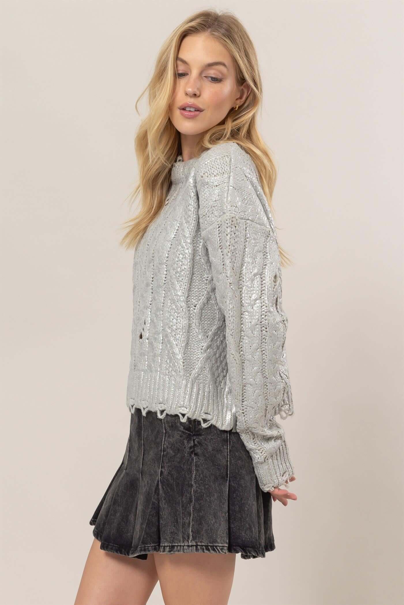 Woman wearing HYFVE distressed cable-knit round neck long sleeve sweater paired with a skirt, showcasing a stylish and casual look.