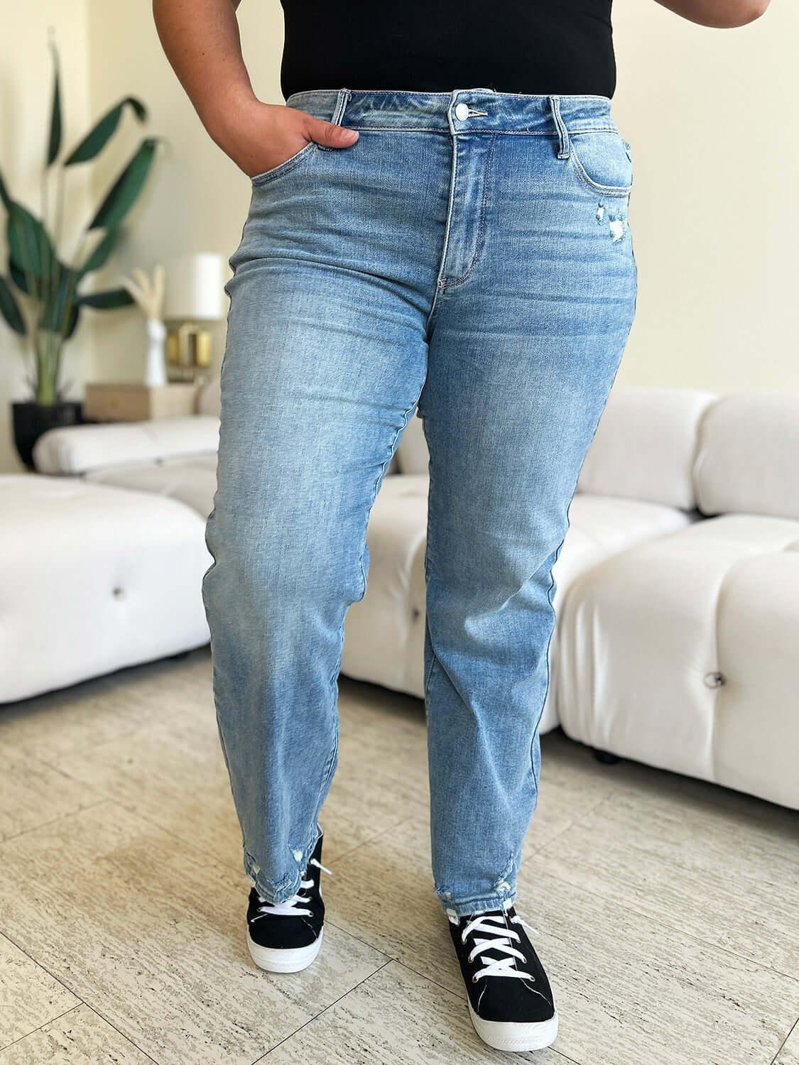 Person wearing High Waist Distressed Straight Jeans by Judy Blue Jeans, styled with black sneakers, standing in a modern living room.