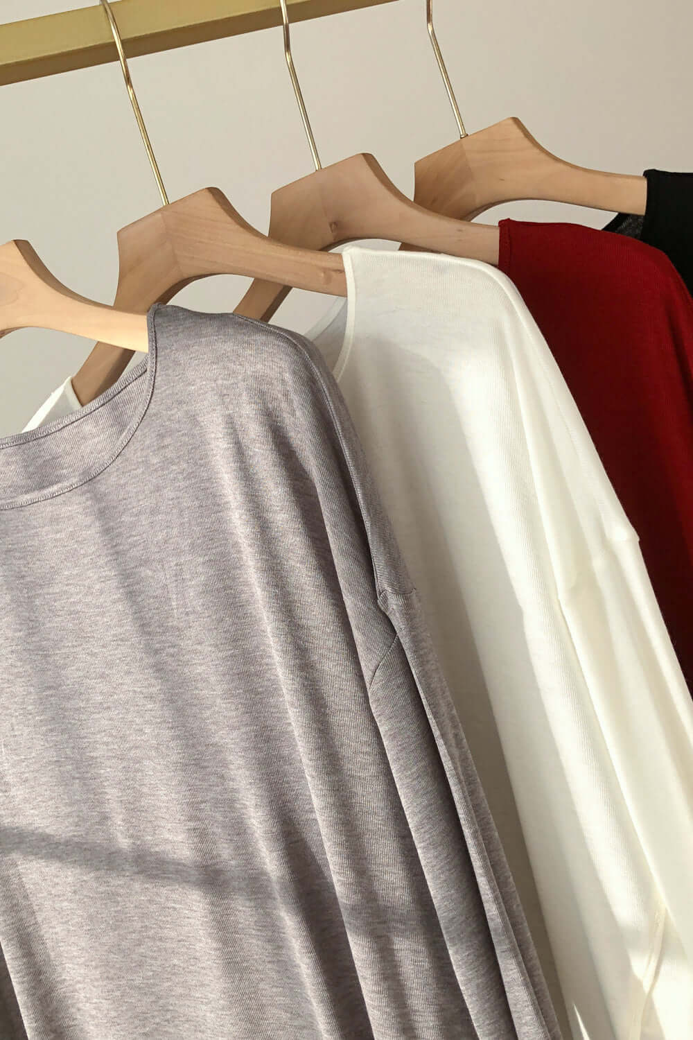 Monochrome and rust Basic Bae High-Low Long Sleeve T-Shirts hanging on wooden hangers. Casual and trendy fashion essentials.