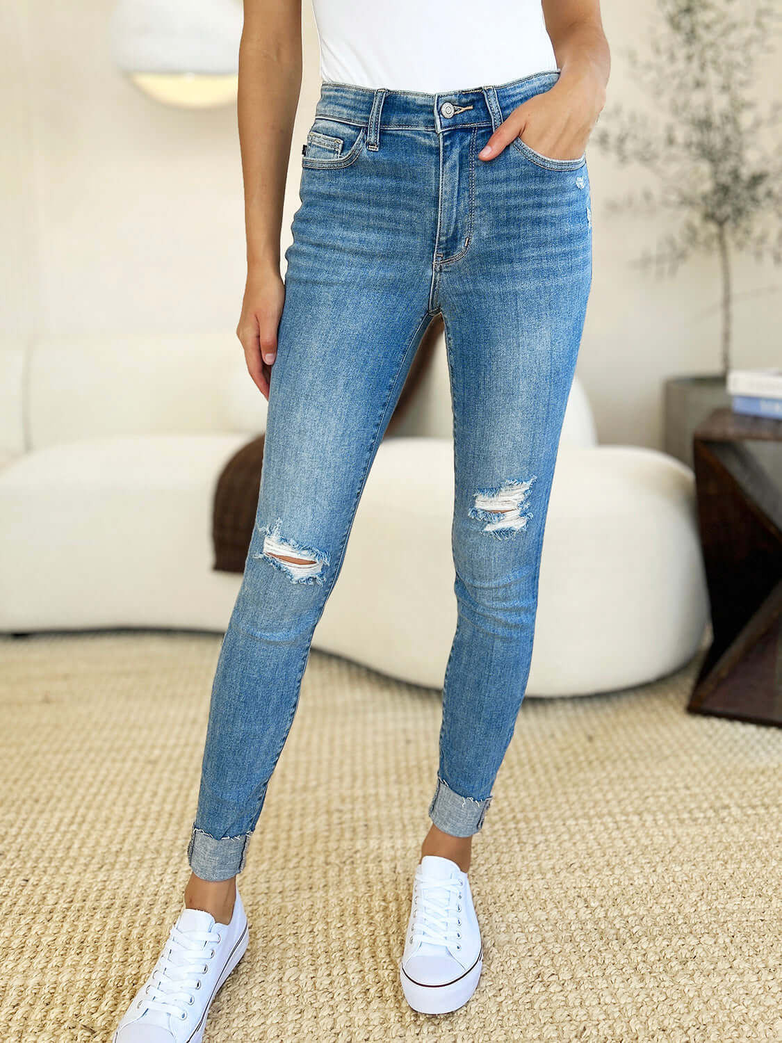 Woman wearing Judy Blue Jeans Mid Rise Destroy & Cuff Skinny Jeans with destroyed detailing and cuffed hem, shown with a white top and sneakers