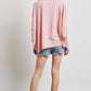 Woman modeling HEYSON garment-dyed oversized boat neck top in pink, paired with denim shorts, showcasing a relaxed, chic style.