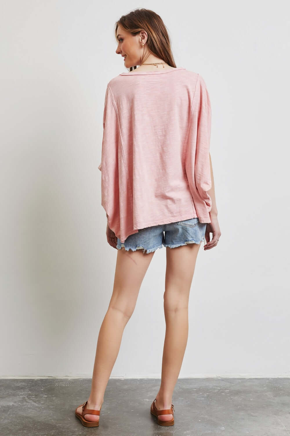 Woman modeling HEYSON garment-dyed oversized boat neck top in pink, paired with denim shorts, showcasing a relaxed, chic style.