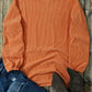 Bella Road Hey Boo Graphic Round Neck Long Sleeve Sweatshirt in orange laid out with jeans, boots, and sunglasses on a wooden surface.