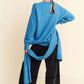 Woman in blue V-neck dropped shoulder sweater with scarf, styled casually with black wide-leg pants and sneakers.