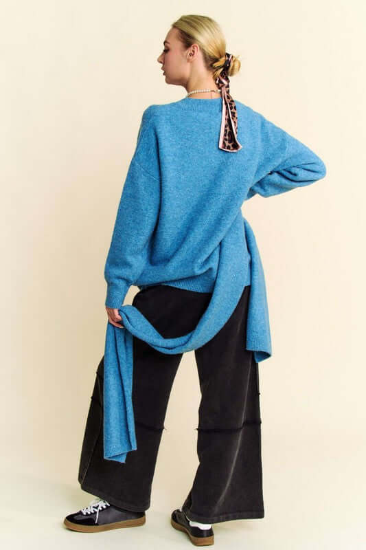 Woman in blue V-neck dropped shoulder sweater with scarf, styled casually with black wide-leg pants and sneakers.