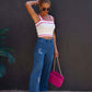 Woman wearing embroidered straight jeans with pockets, white tank top, and holding pink handbag.