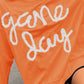 Bella Road Game Day Round Neck Long Sleeve Sweatshirt in orange with "game day" text, worn by a smiling woman