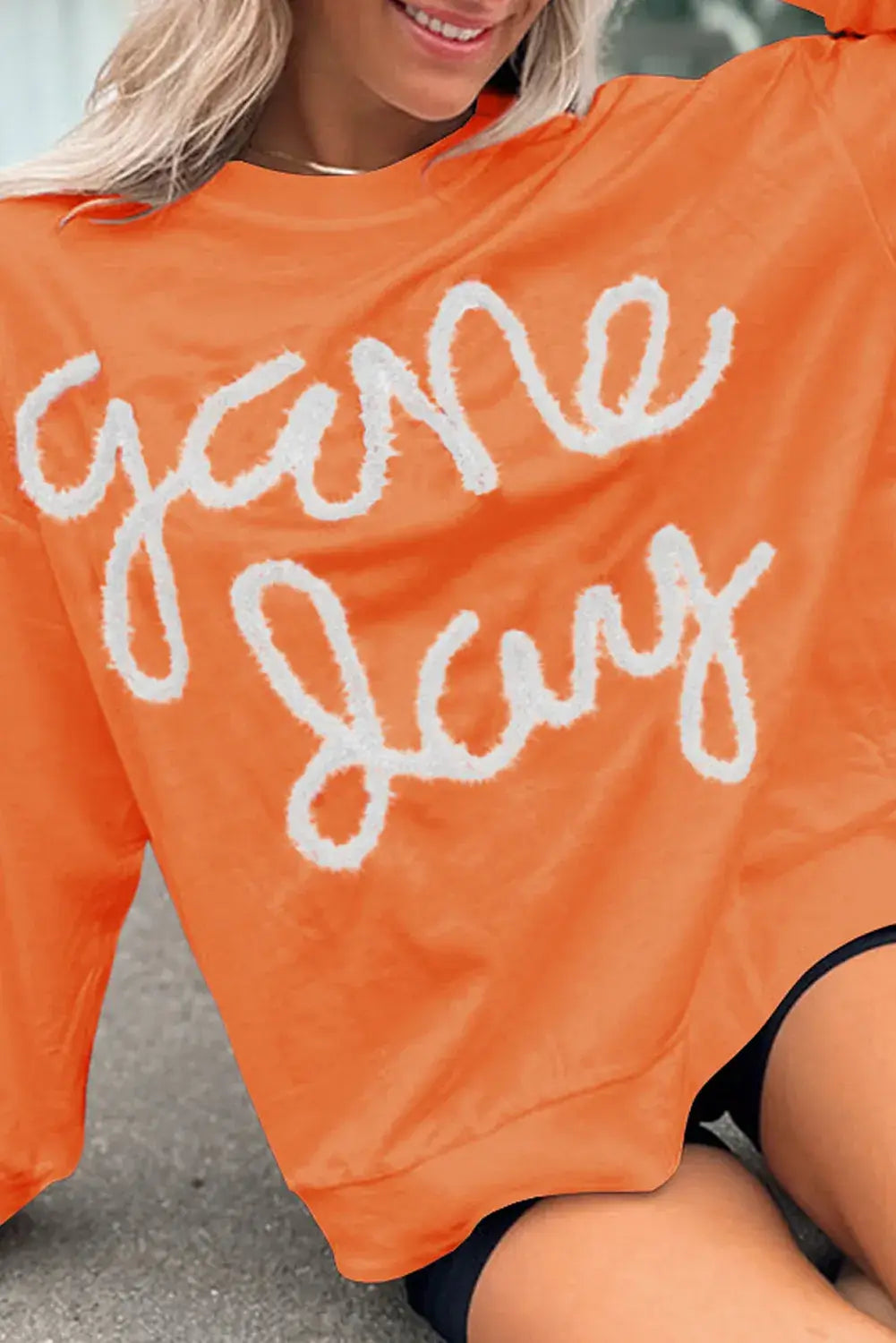 Bella Road Game Day Round Neck Long Sleeve Sweatshirt in orange with "game day" text, worn by a smiling woman