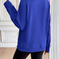 Woman wearing Ivy Lane Half Zip Raglan Sleeve Sweatshirt in blue, viewed from the back with her hand touching the collar in a stylish setting.