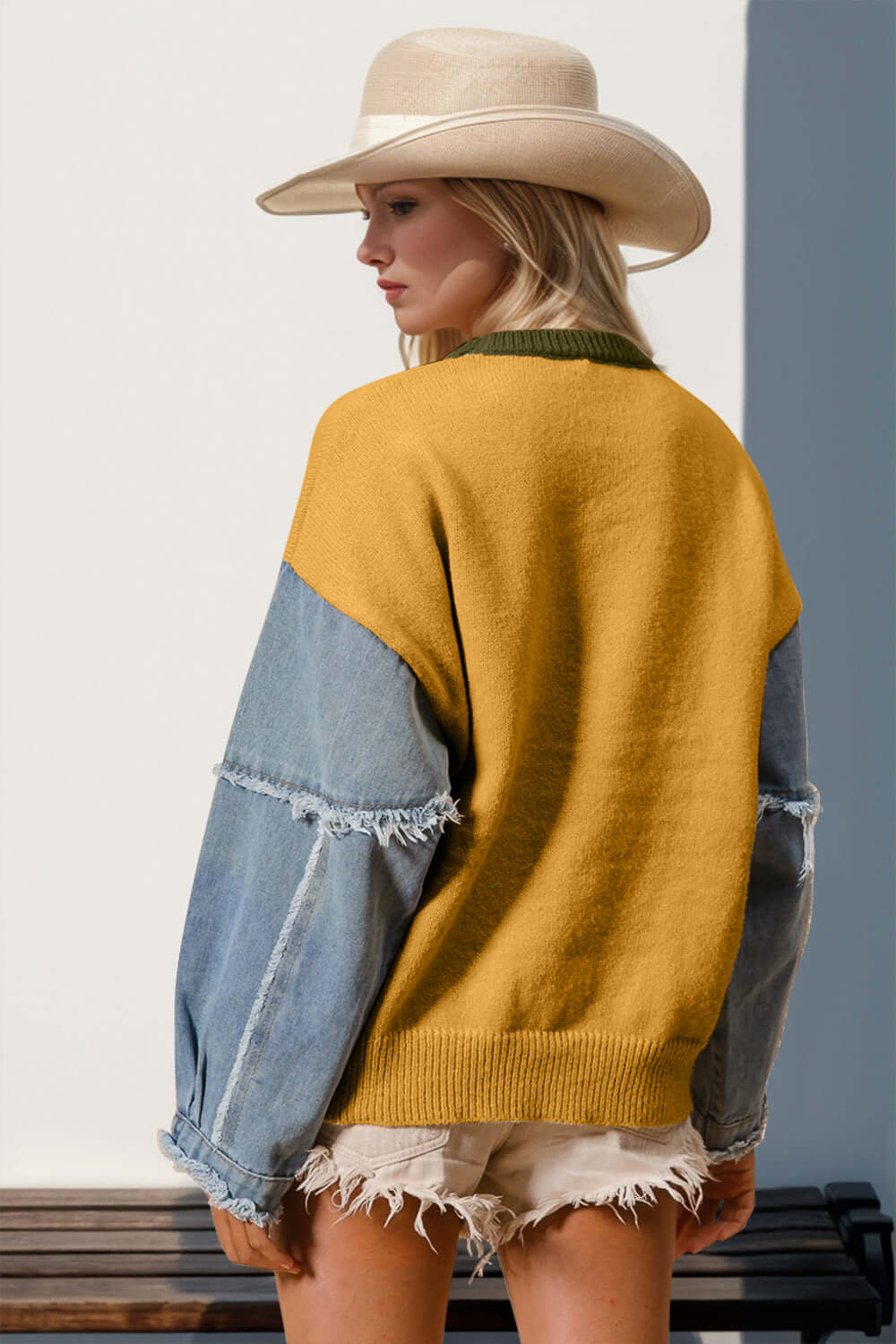 Trendy woman in a mustard yellow and denim raw edge sweater with a hat, showcasing unique fashion style from behind.