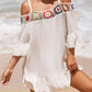 Woman wearing crochet cold shoulder three-quarter sleeve cover-up with ruffled sheer and floral design on beach.