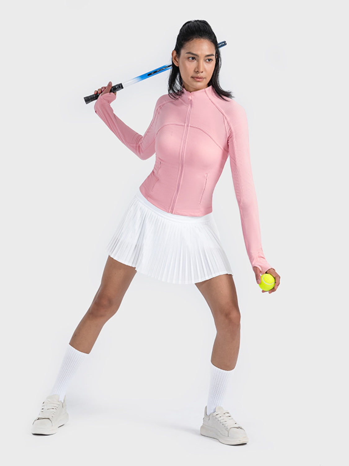 Model in a pink zip-up long sleeve sports jacket with a tennis racket and ball, ready for action in sporty style.