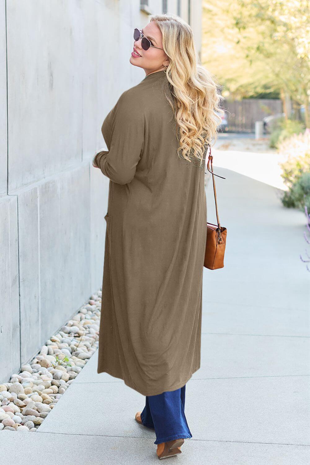 Woman wearing open front long sleeve cover up with pocket and sunglasses, showcasing lightweight outerwear, walking on a pathway