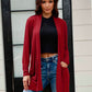 Woman wearing a red open front long sleeve cardigan with pockets over a black top and jeans.