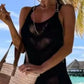 Woman in a black fringe cover-up holding a beach bag, enjoying a sunny day by the ocean. Perfect summer style!