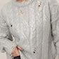 Woman wearing a stylish distressed cable-knit sweater with a round neck design, perfect for casual spring or autumn fashion.