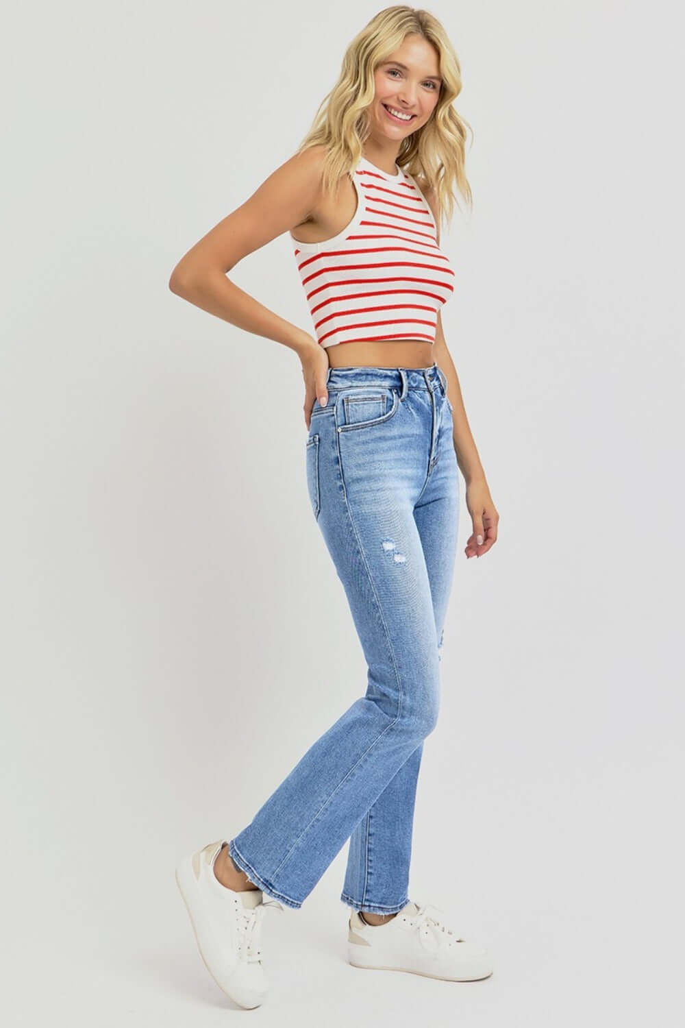 Woman wearing RISEN distressed high-rise ankle straight jeans with a striped tank top, showcasing casual and trendy style.