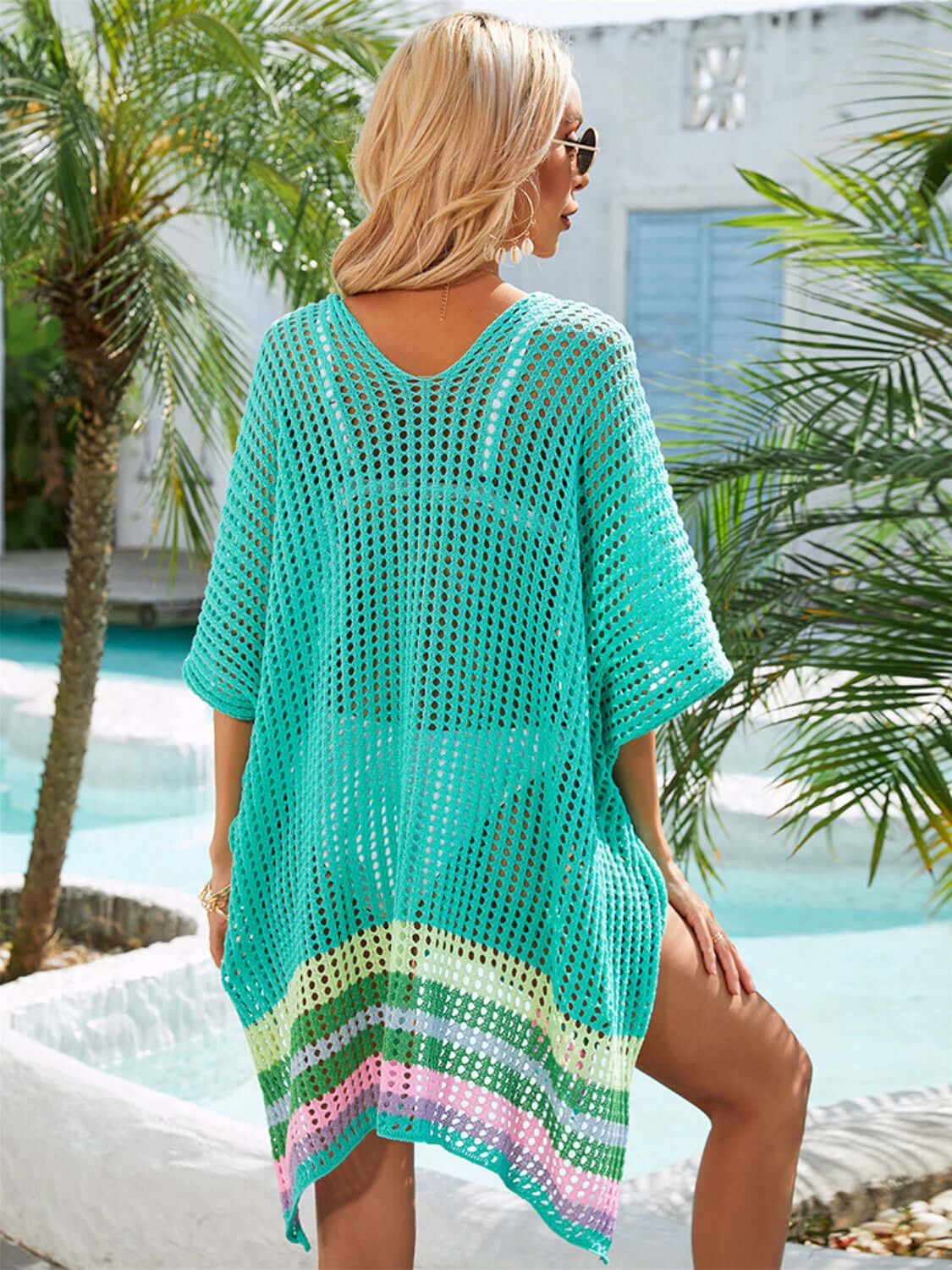 Woman wearing a teal slit openwork V-neck half sleeve cover-up by the pool with palm trees in the background