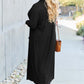 Woman modeling black open front long sleeve cover up with pockets, outdoors, wearing sunglasses and holding a brown bag.