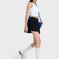 Stylish woman in a white crop top and black pleated active skirt, accessorized with a cap and sporty shoes.