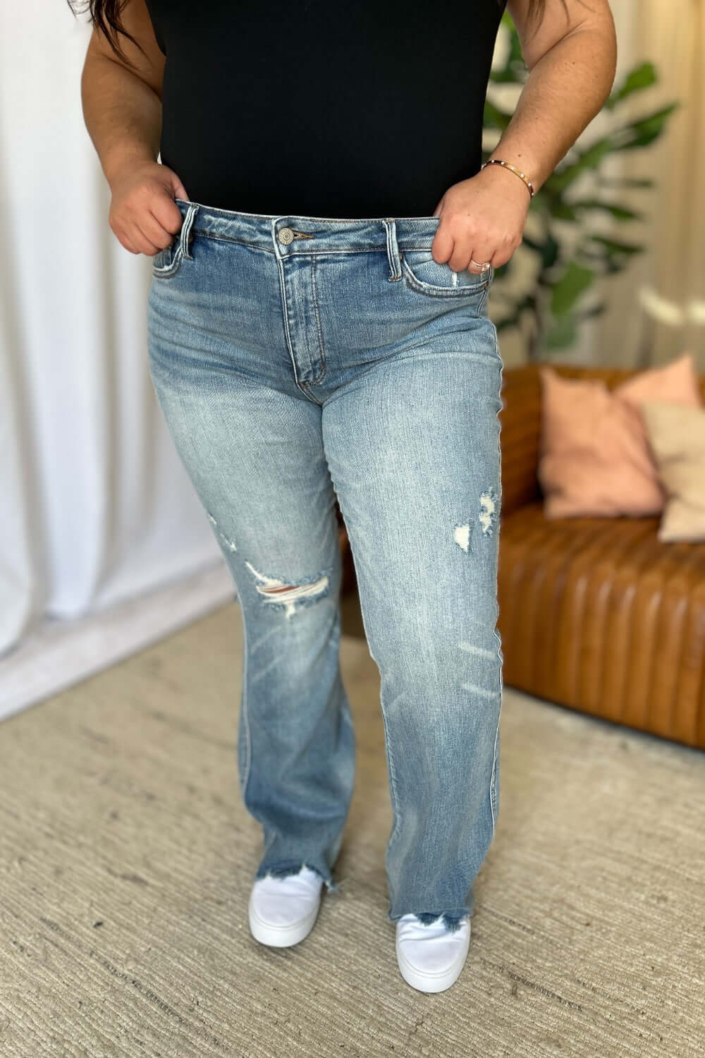 Woman wearing Judy Blue full size medium rise tummy control destroy flare jeans with distressed detailing, standing indoors.