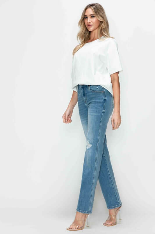 Model in distressed high rise straight jeans paired with a chic white top and trendy heels, showcasing stylish denim fashion.