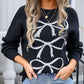 Woman wearing black round neck long sleeve sweater with white bow graphic design, paired with light-wash jeans and gold necklaces