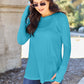 Woman wearing round neck long sleeve teal t-shirt with jeans outdoors.