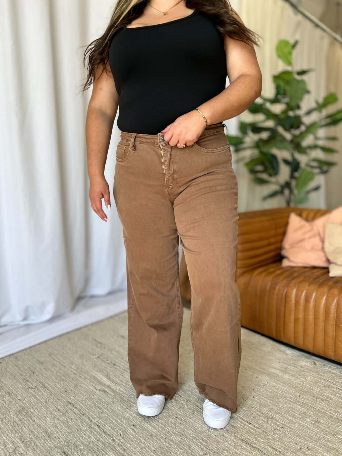 Woman wearing RFM High Rise Garment Dye Wide Leg Jeans with black top, standing in a stylish living room.