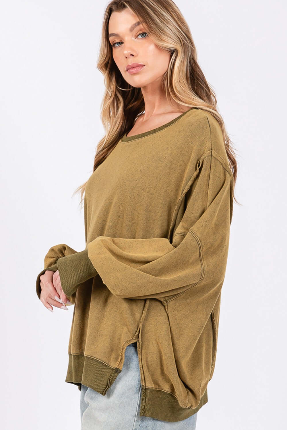 Woman wearing an oversized mineral wash side slit sweatshirt with a scoop neck and exposed seams, showcasing a comfortable and stylish look.