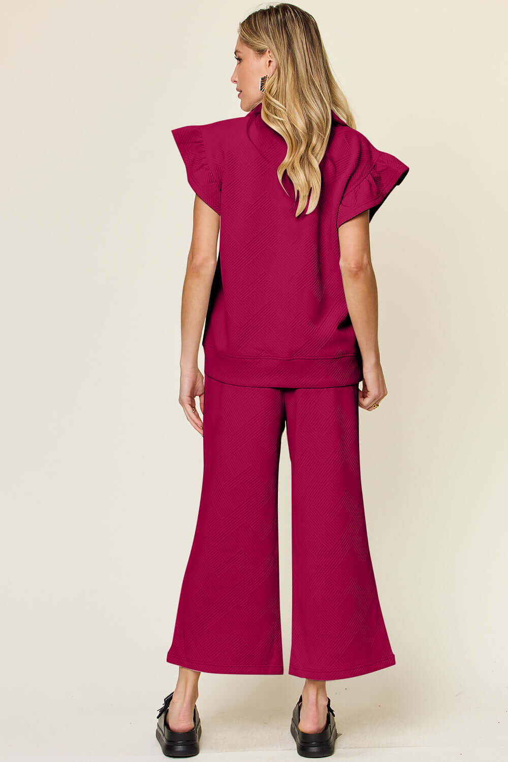 Woman wearing fuchsia texture ruffle short sleeve top and drawstring wide leg pants set, viewed from the back.