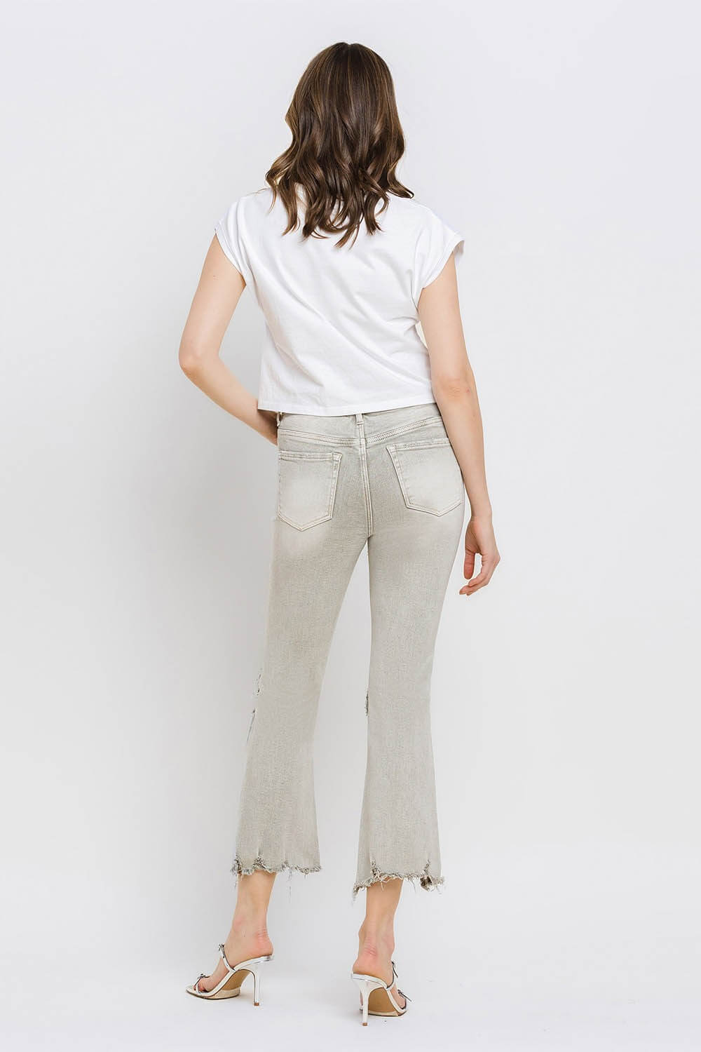 Woman wearing Lovervet distressed raw hem cropped flare jeans with a white top and heels, showcasing the back view of the jeans.