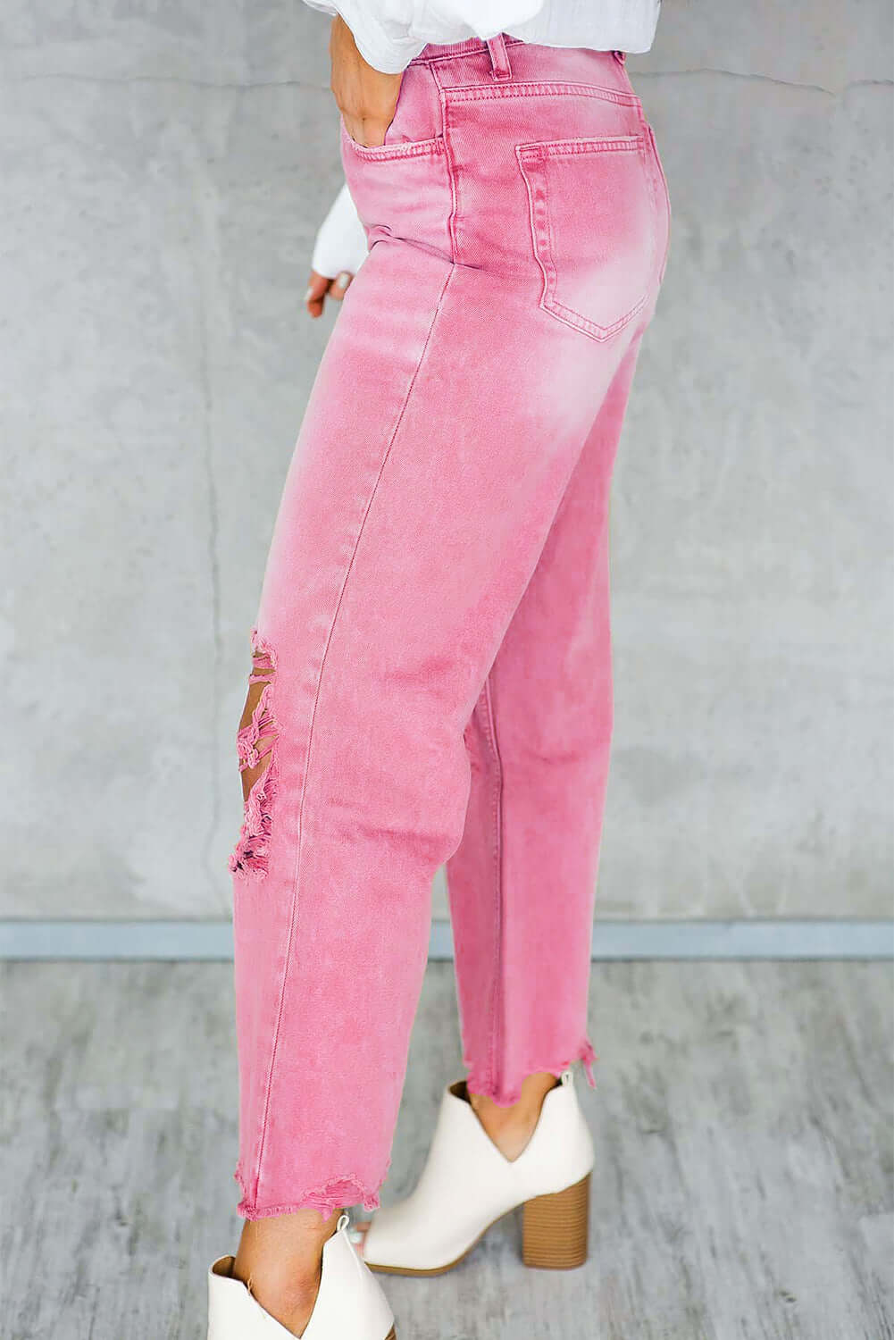 Woman wearing pink distressed raw hem jeans with pockets and white ankle boots.