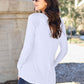 Woman wearing white round neck long sleeve t-shirt, shown from the back, standing outdoors in a casual setting.