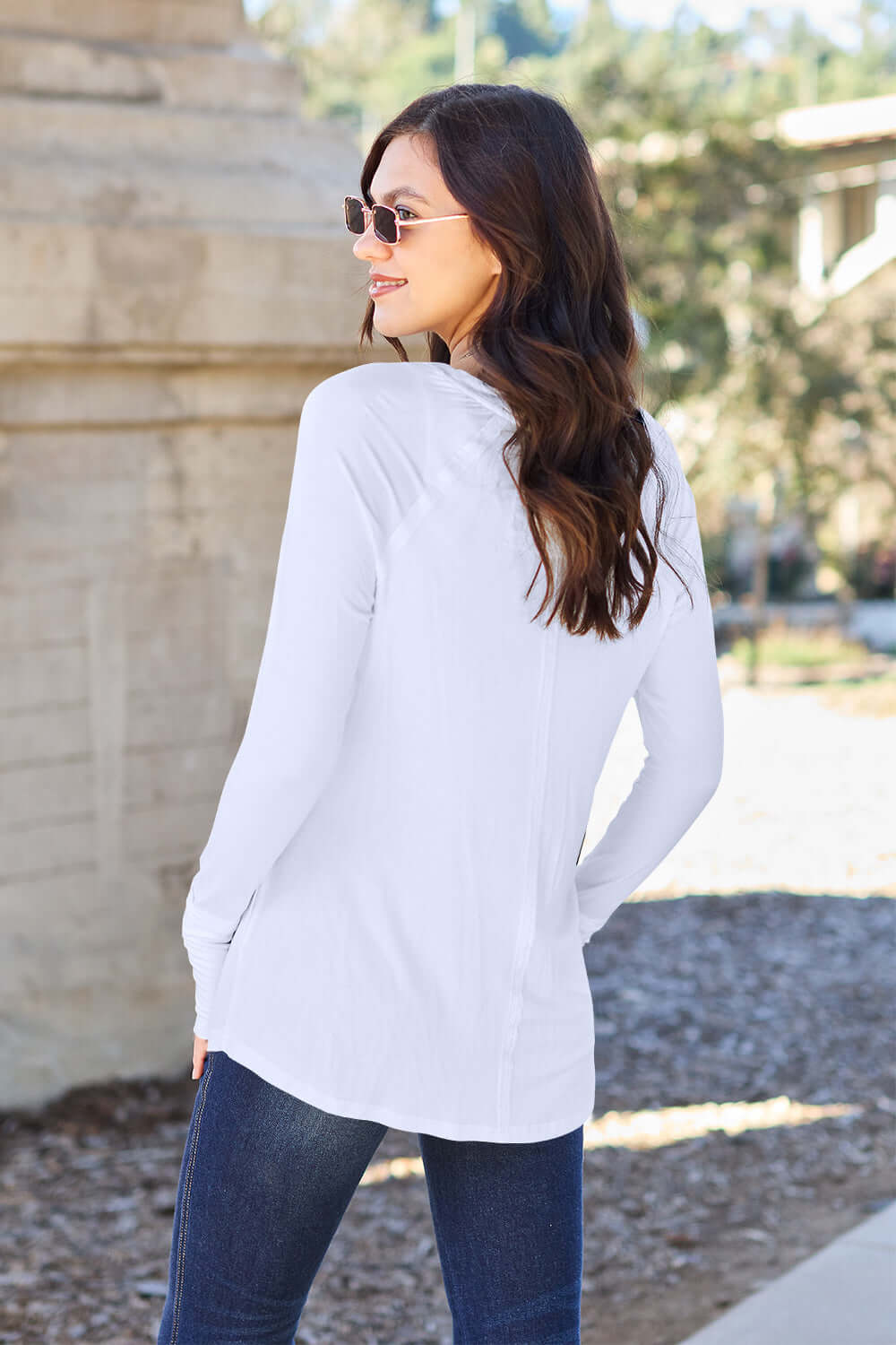 Woman wearing white round neck long sleeve t-shirt, shown from the back, standing outdoors in a casual setting.