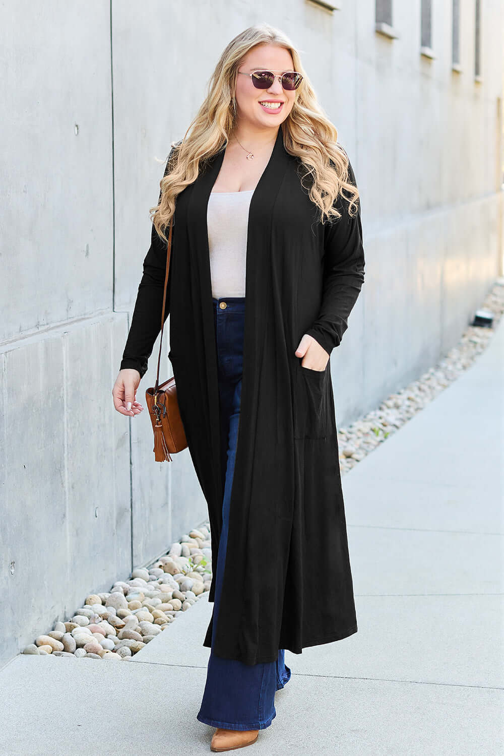 Woman wearing black open front long sleeve cover up over white top and blue jeans, accessorized with sunglasses and crossbody bag, walking