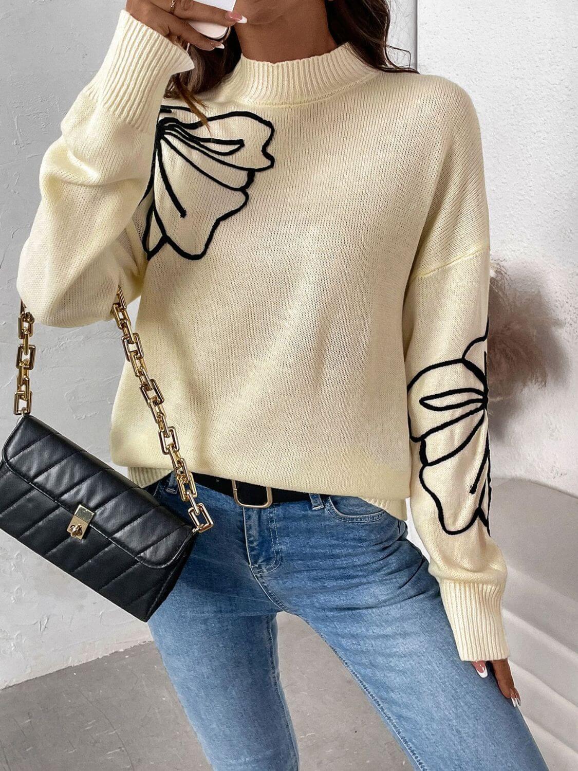 Woman wearing Perfee Mock Neck Dropped Shoulder Long Sleeve Sweater in cream with floral design and black quilted handbag