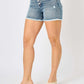 Woman wearing Button Fly Raw Hem Denim Shorts from Judy Blue Jeans with a button fly closure and raw hem detail.