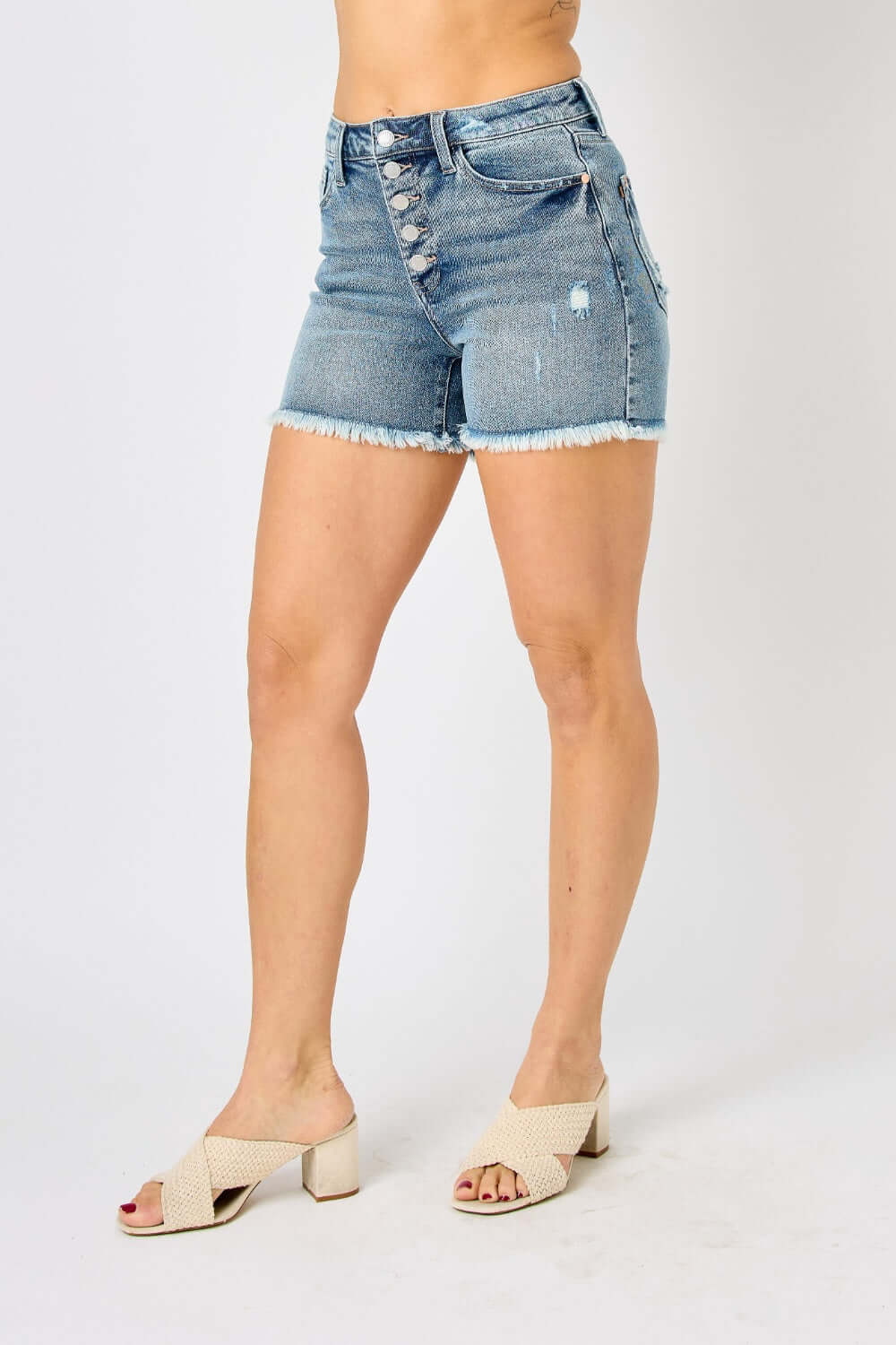 Woman wearing Button Fly Raw Hem Denim Shorts from Judy Blue Jeans with a button fly closure and raw hem detail.