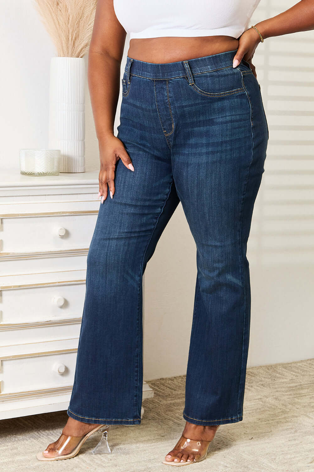 Woman wearing Judy Blue Jeans elastic waistband slim bootcut full size jeans in dark wash, paired with a white crop top.