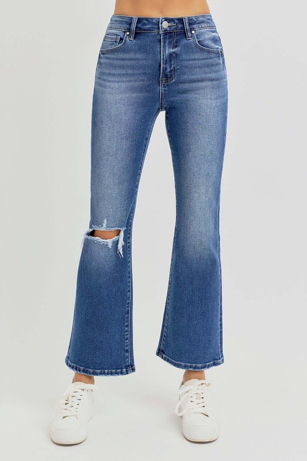 Trendy distressed high rise crop flare jeans with ripped knee detail, styled with white sneakers for a chic and modern look.