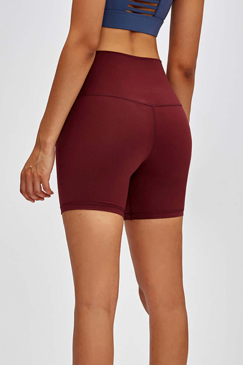 Model showcasing burgundy Millennia high-waist training shorts with a hidden pocket and 5’ inseam from the back.