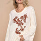 Model showcasing the POL Embroidered Round Neck Long Sleeve Knit Top with floral design on a neutral background.