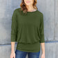 Woman wearing green round neck batwing sleeve top with jeans against concrete wall.