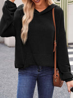 Woman wearing a black textured kangaroo pocket long sleeve hoodie, paired with blue jeans and a brown crossbody bag.